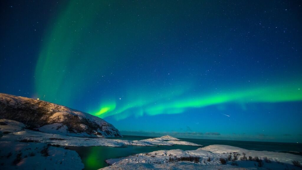 Aurora boreal sobre montanhas nevadas em Tromsø, na Noruega